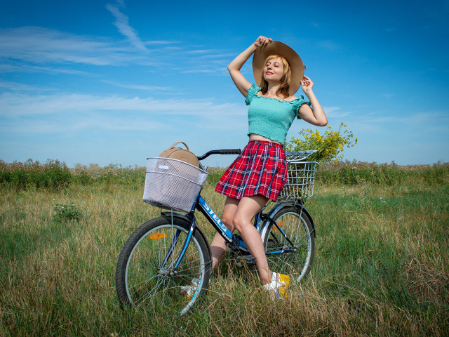 Молодая девушка на велосипеде на поле под голубым небом 
