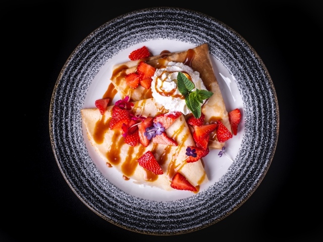 Блины со сливками и ягодами в тарелке на черном фоне