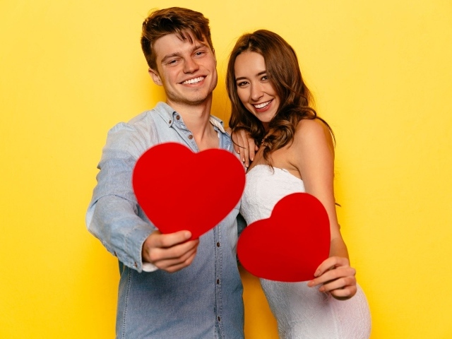 Влюбленная пара на желтом фоне с бумажными сердечками в руках 