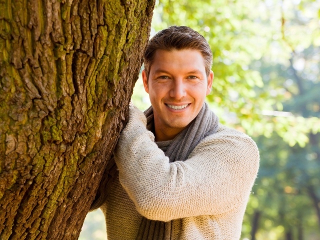 Улыбающийся мужчина стоит у дерева 