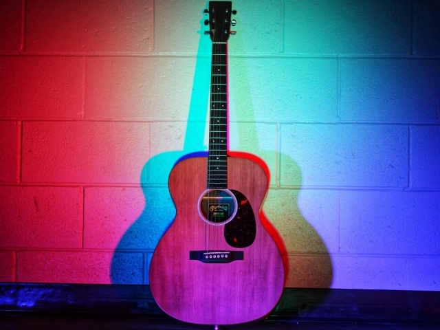 Гитара стоит у стены в разноцветном свете 