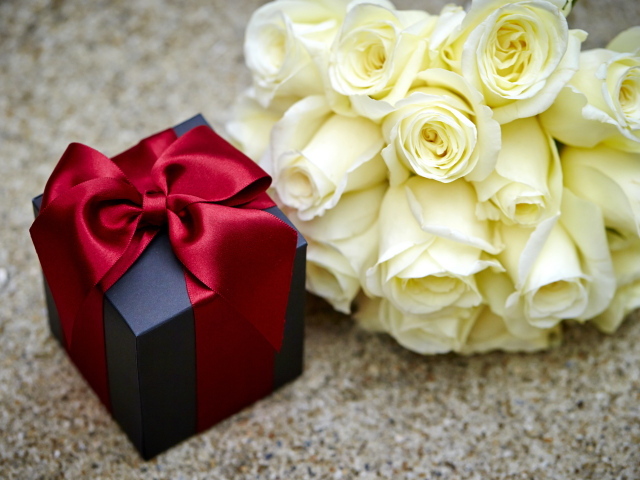 Букет белых роз с черным подарком на столе