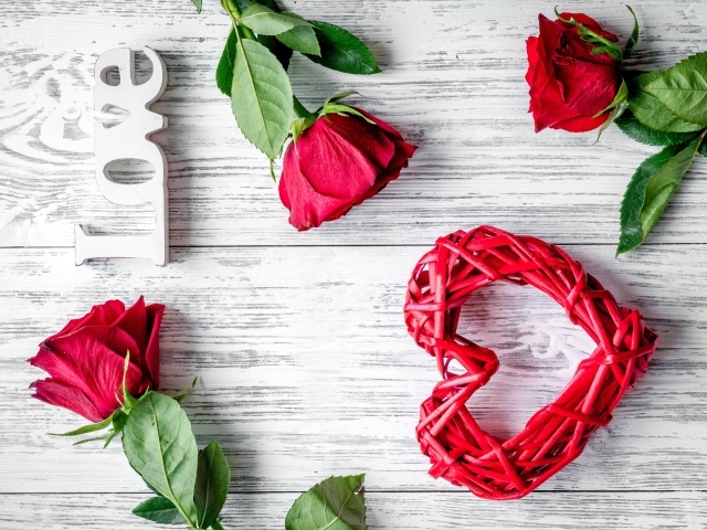 Красное плетеное сердце с алыми розами на деревянном столе