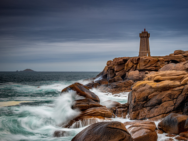 Старая башня маяка на каменном берегу у моря 