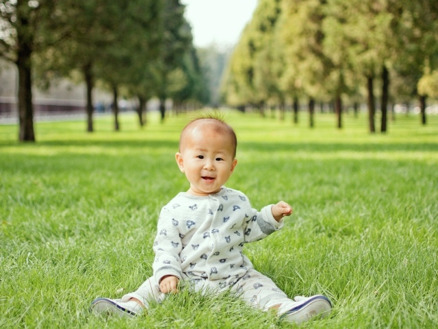 Маленький ребенок азиат сидит на зеленой траве 