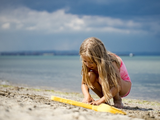 Маленькая девочка блондинка играет на песке у моря