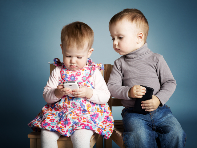 Маленькие мальчик  и девочка с телефонами на сером фоне 