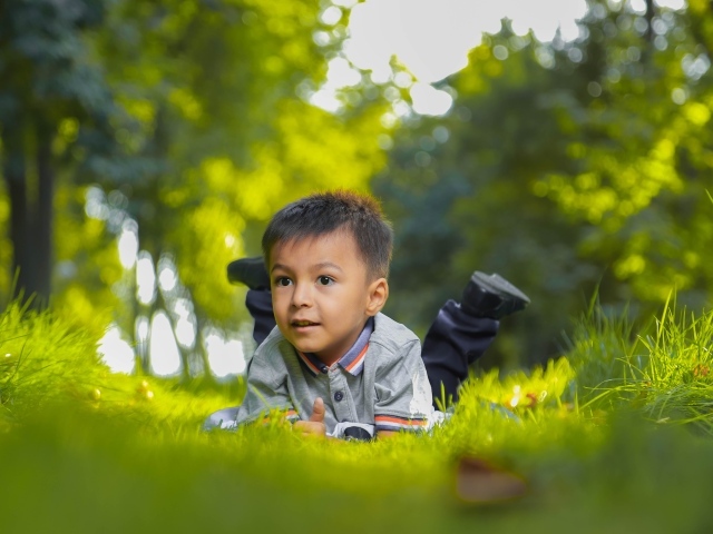 Маленький мальчик лежит на зеленой траве 