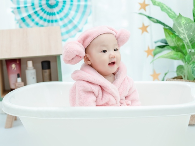 Маленький ребенок в розовом халате сидит в белой ванной