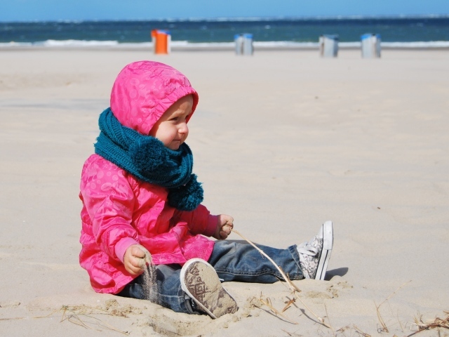 Маленькая девочка в розовой куртке на песке