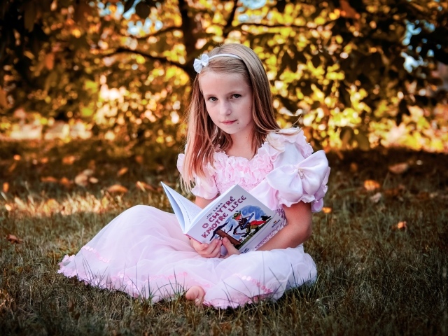 Маленькая принцесса сидит на траве с книгой