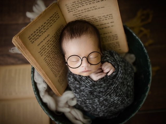 Маленький спящий ребенок в ведре с книгой 