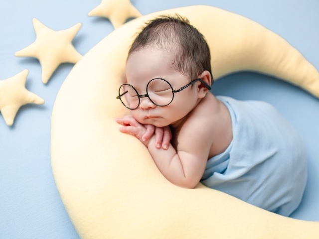 Спящий ребенок в очках на подушке в форме месяца