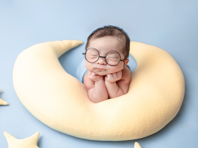Спящий грудной ребенок в очках на желтой подушке 