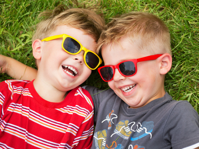 Два улыбающихся мальчика в очках на зеленой траве 
