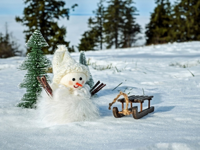 Игрушечный снеговик с санками стоит на снегу 