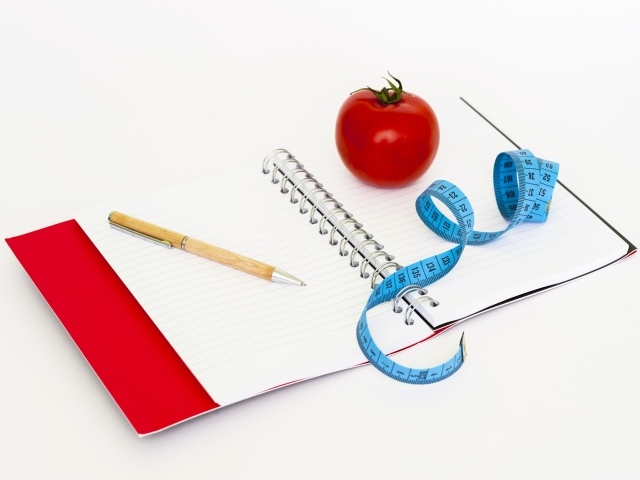 Блокнот с ручкой на столе с сантиметром и помидором