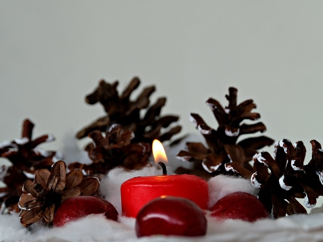 Красная зажженная свеча с шишками на сером фоне