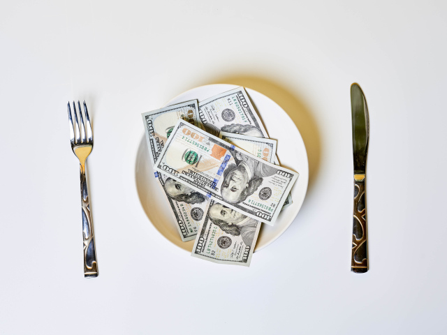 Доллары на тарелке на сером фоне со столовыми приборами