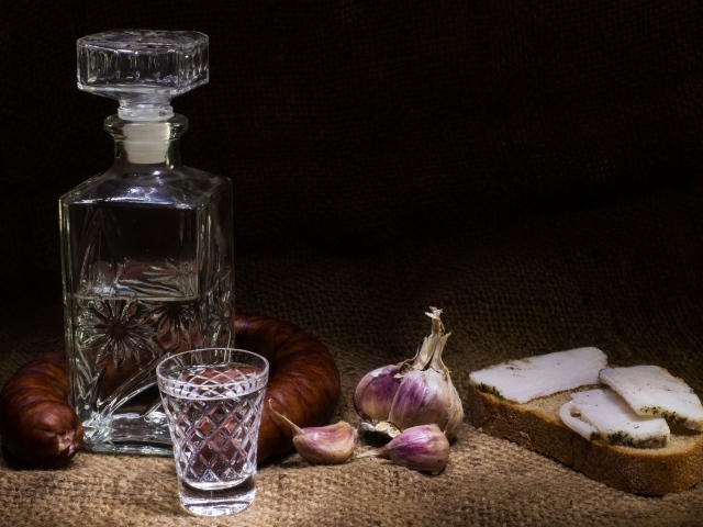 Бутылка водки на столе с салом, колбасой и чесноком