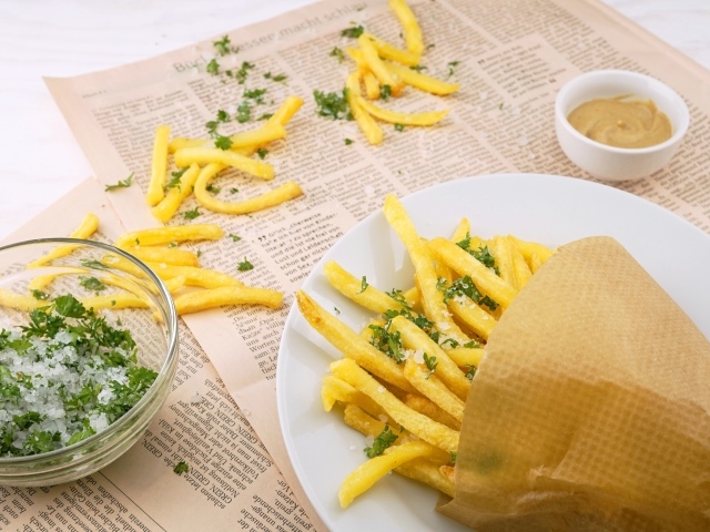 Картофель фри на столе с газетой, солью и зеленью 