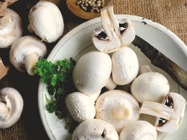 Свежие шампиньоны на тарелке на столе
