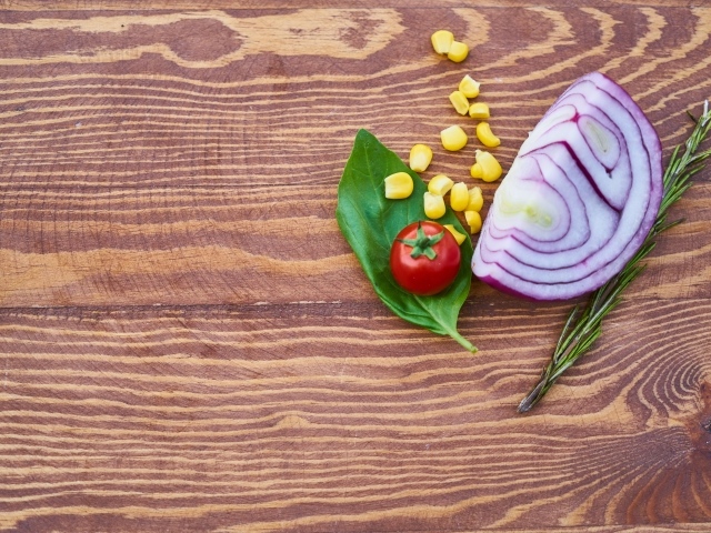 Половина лука на столе с кукурузой и помидором