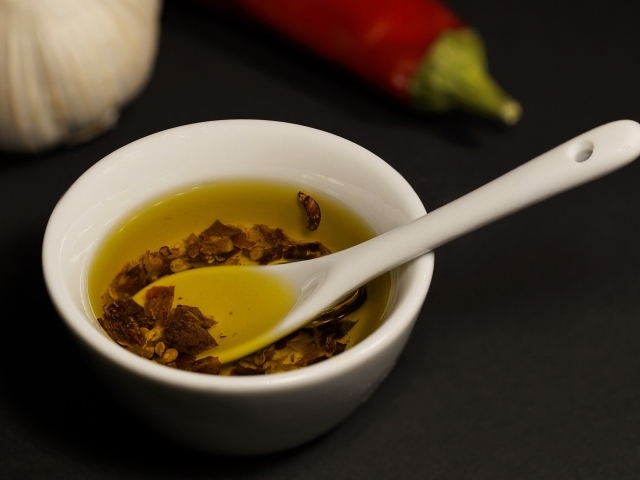 Оливковое масло в тарелке на столе с перцем и чесноком