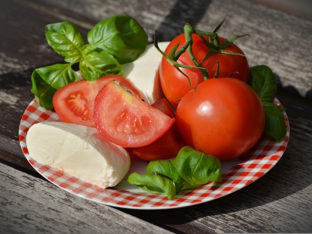 Красные помидоры с сыром и базиликом на тарелке