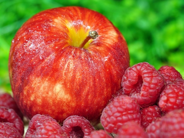 Большое красное яблоко лежит с ягодами малины