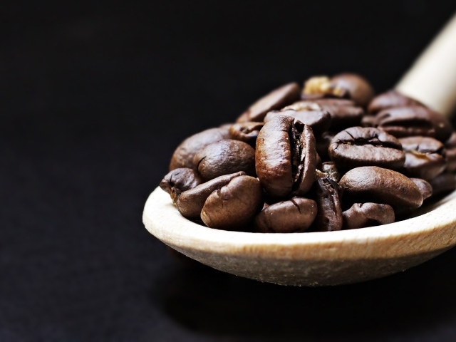 Зерна кофе на деревянной ложке на черном фоне