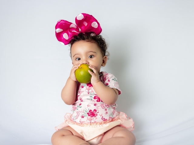 Девочка с большим бантом на голове ест апельсин