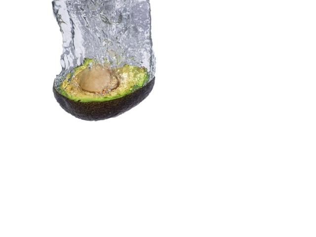 Половина авокадо падает в воду на белом фоне