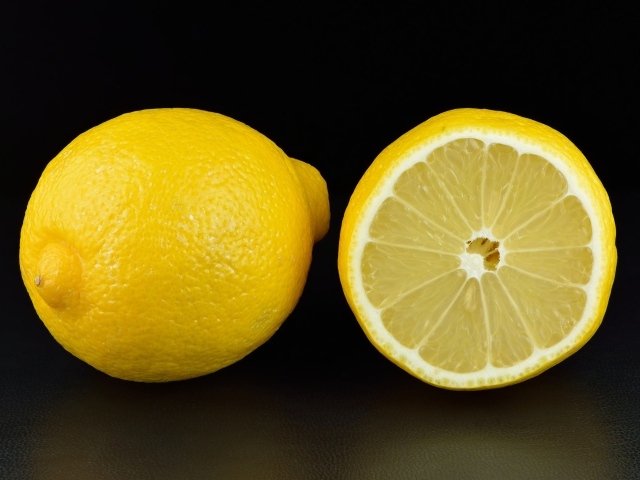 Большой желтый лимон с половиной на черном фоне