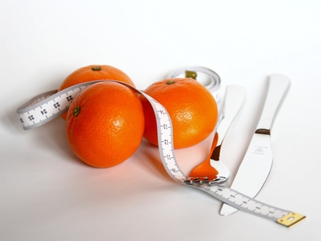 Мандарины с сантиметром и столовыми приборами на белом фоне