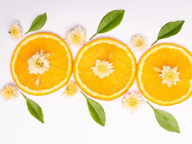 Три кружочка апельсина на белом фоне с цветами и зелеными листьями
