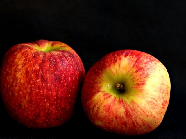 Два больших спелых красных яблока на черном фоне