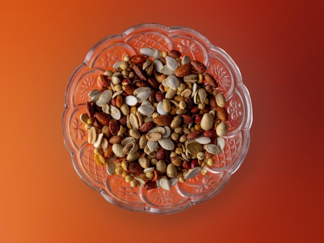 Разные орехи в стеклянной посуде на оранжевом фоне