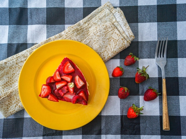 Кусок чизкейка с клубникой на желтой тарелке 