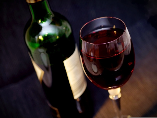 Бутылка красного вина с бокалом на столе