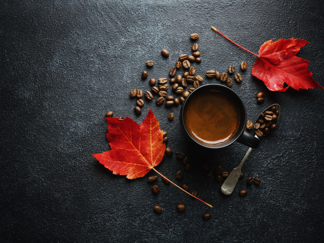 Чашка кофе на столе с зернами и желтыми листьями