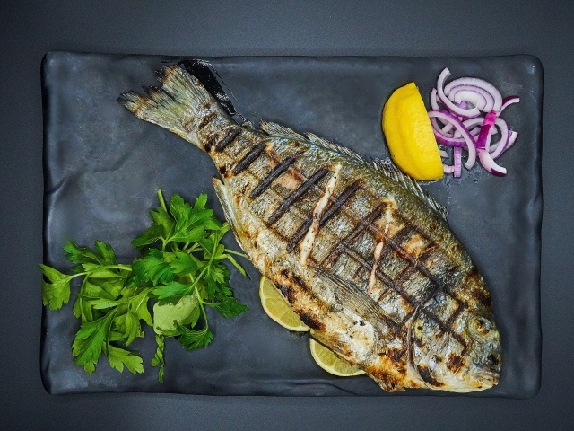 Жареная рыба с лимоном, луком и петрушкой на тарелке