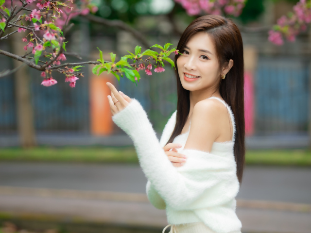 Красивая азиатка в белом свитере стоит у ветки дерева