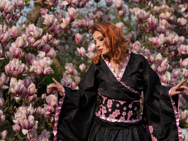 Девушка в кимоно стоит у куста с цветами магнолии