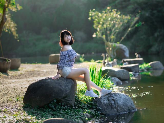 Девушка сидит на большом камне у пруда
