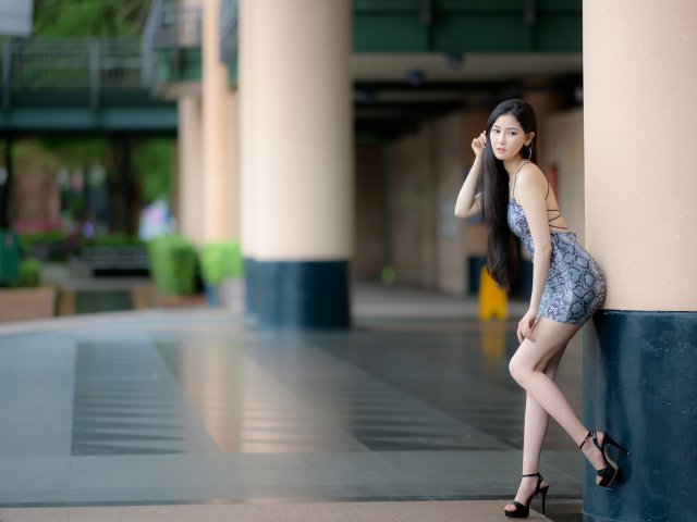Стройная азиатка в коротком платье  стоит у колонны