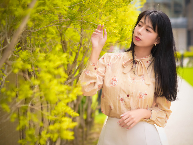 Молодая девушка азиатка стоит у дерева с зелеными листьями
