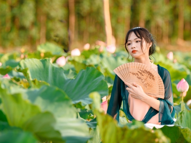 Девушка азиатка с веером в зеленых листьях лотоса