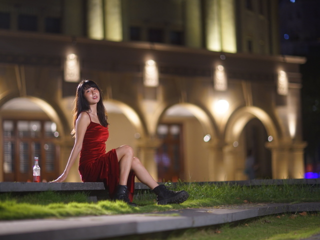 Азиатка в длинном красном платье сидит на ступенях