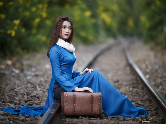 Красивая девушка азиатка сидит на рельсах с чемоданом